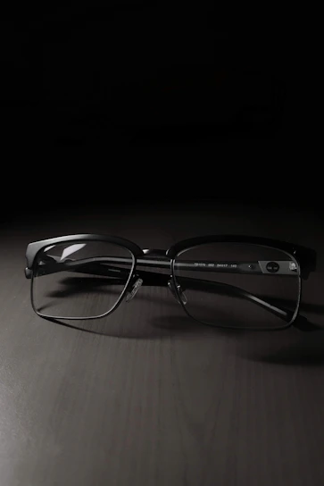Close-up of sleek black optical frames resting on a white surface with subtle deep blue accents.