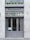 A stylish storefront with a gray painted facade and large glass doors. Above the doors, there is an awning and signage reading 'Monsieur P.' A row of neatly trimmed green shrubs in pots decorates the upper ledge.