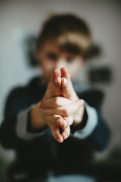 A child's hands are held together in a playful or imaginative gesture, with the focus on the fingers. The background is blurred, highlighting the hands in the foreground.