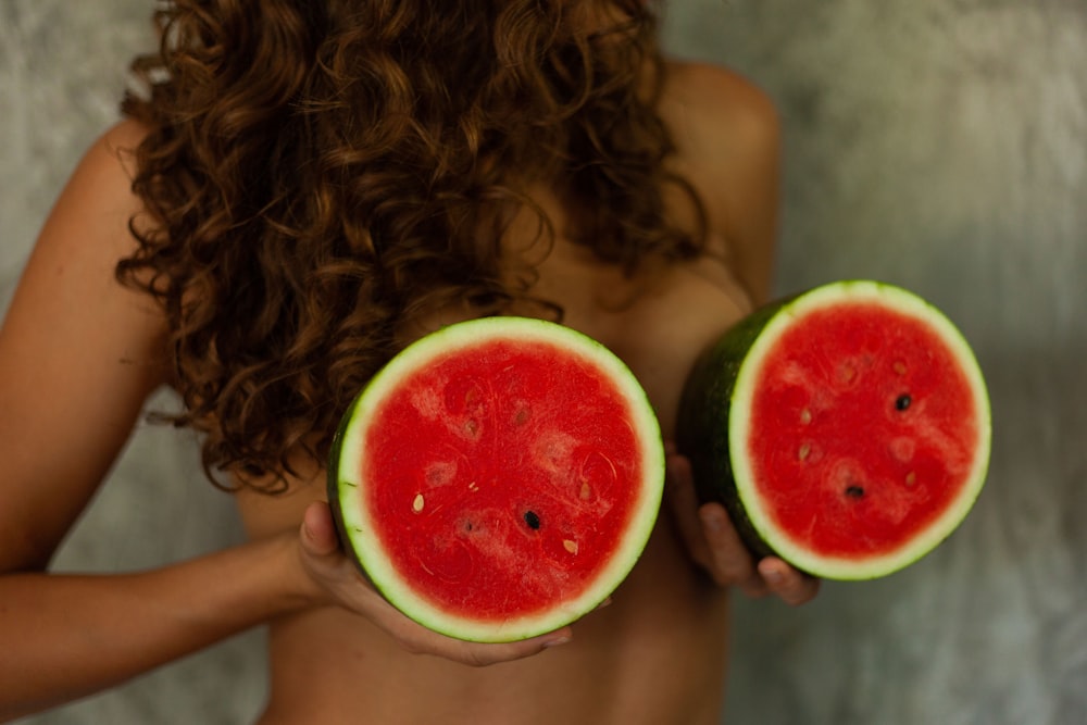 A person holding sliced watermelon fruit in front of their breasts.