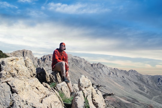 man in red jacket sitting on rock formation during daytime in Tikjda Algeria