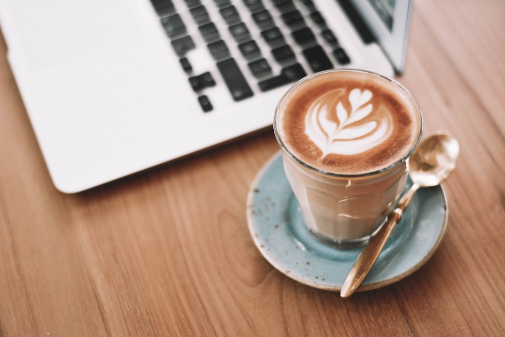 Tasse en céramique blanche sur soucoupe à côté du MacBook Pro