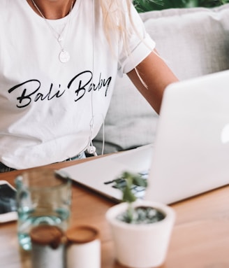 woman in white crew neck t-shirt sitting by the table with macbook