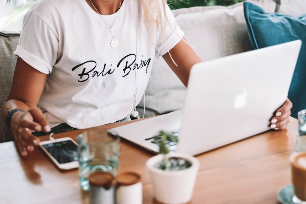 woman in white crew neck t-shirt sitting by the table with macbook