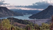 A panoramic view of a large dam and reservoir surrounded by green hills.