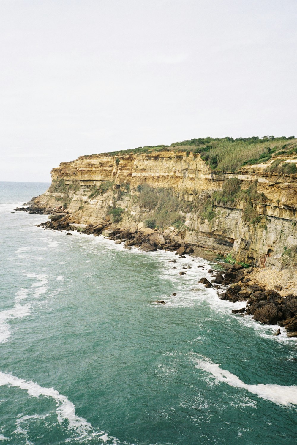 brown and green cliff beside sea during daytime