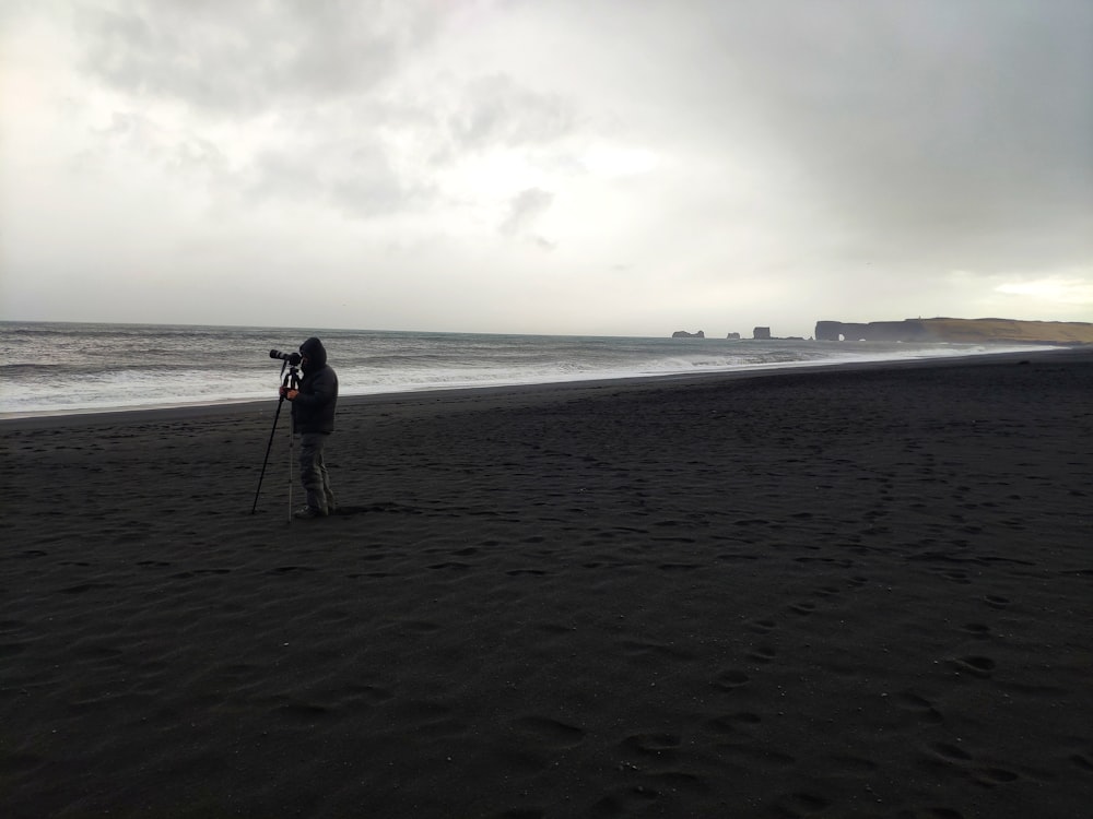 검은 재킷과 파란색 데님 청바지를 입은 남자가 낮 동안 해변에 서 있다