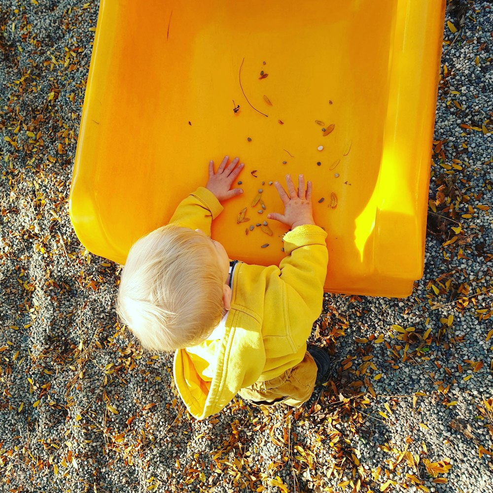 Kind in gelbem Langarmhemd und Hose spielt auf gelbem Plastikbehälter