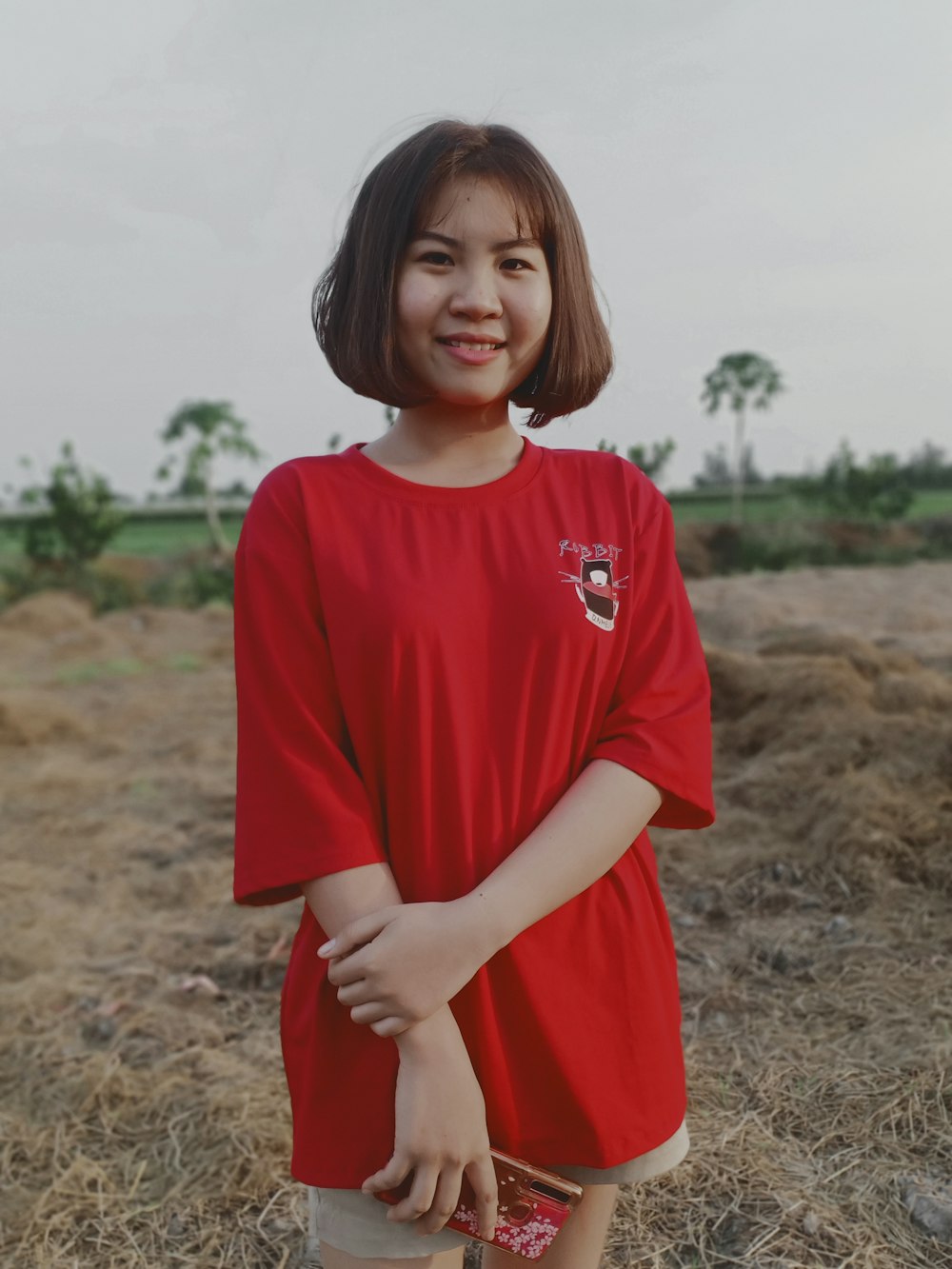 Mujer con camiseta roja de cuello redondo de pie en el campo marrón durante el día