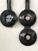 Three black circular electrical fixtures mounted on a light wall. The top-left fixture is a plug socket labeled 'Berker', while the other two have central buttons or lights.