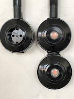 Three black circular electrical fixtures mounted on a light wall. The top-left fixture is a plug socket labeled 'Berker', while the other two have central buttons or lights.