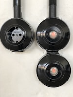 Three black circular electrical fixtures mounted on a light wall. The top-left fixture is a plug socket labeled 'Berker', while the other two have central buttons or lights.