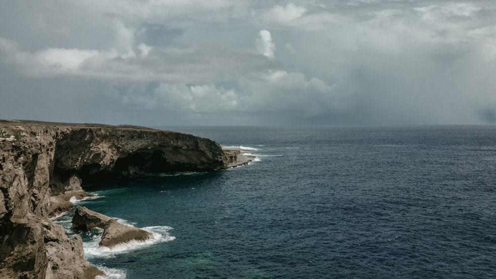 brown rock formation on sea under white clouds during daytime