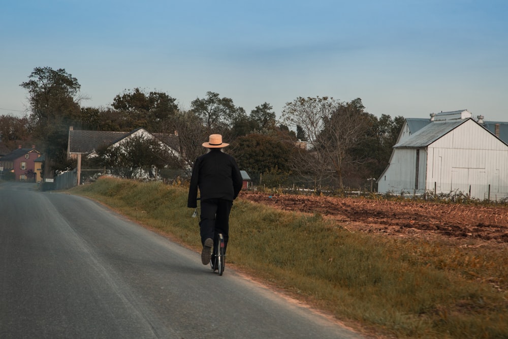 homem em jaqueta preta e calças pretas andando na estrada durante o dia