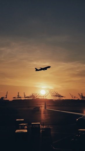 silhouette of airplane flying over the people during sunset