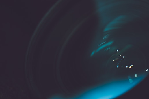 Close-up of a sleek, modern lens reflecting teal and white light with subtle glass transparency effects.