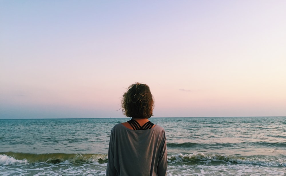 woman in gray shirt standing on seashore during daytime