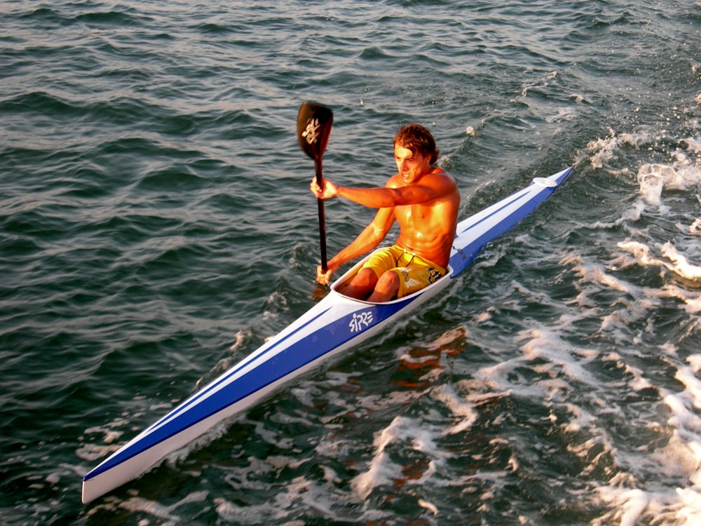 woman in blue and white kayak on body of water during daytime