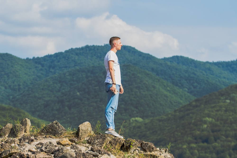 man in white t-shirt and blue denim jeans standing on rock during daytime