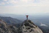 A happy traveler standing atop a mountain peak, arms raised in triumph against a golden sky.