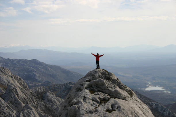 Happy traveler standing on a mountain peak with arms wide open at sunrise.