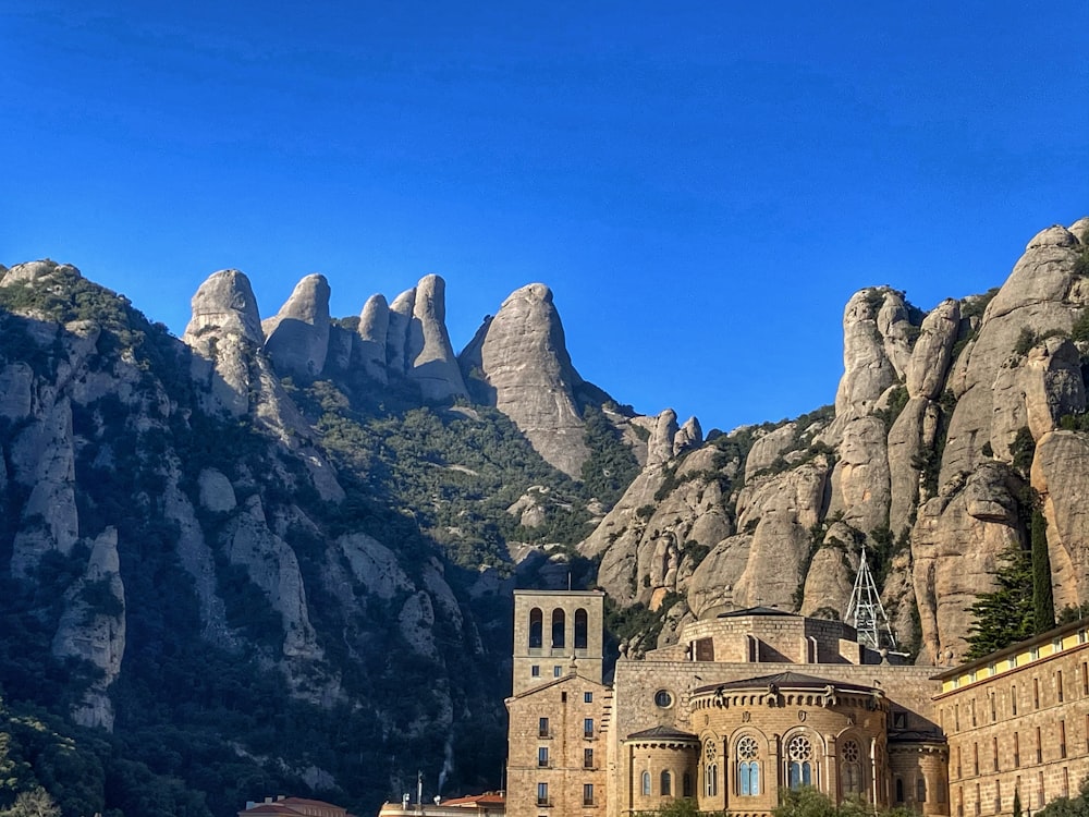 Edificio de hormigón marrón cerca de la montaña rocosa gris bajo el cielo azul durante el día