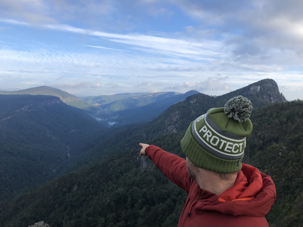 person in orange jacket wearing green knit cap standing on top of mountain during daytime