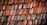 Weathered wooden shingles arranged in a layered pattern, displaying various shades of red and gray due to aging and exposure to the elements.