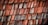 Weathered wooden shingles arranged in a layered pattern, displaying various shades of red and gray due to aging and exposure to the elements.