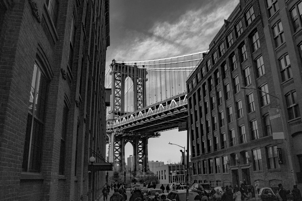 grayscale photo of people walking on street near bridge