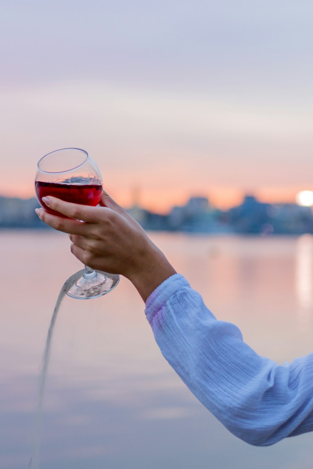 person holding clear wine glass with red liquid