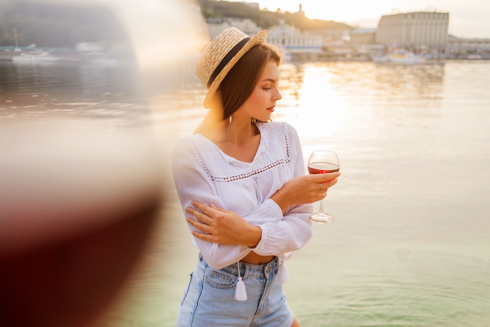 woman in white tank top and blue denim shorts holding white ceramic mug