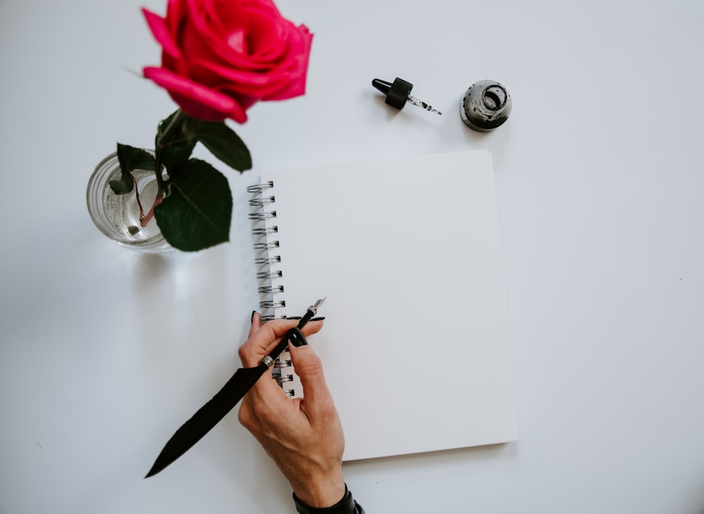 person holding black pen writing on white notebook