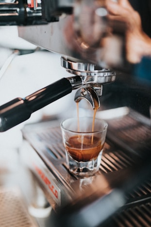 clear drinking glass with brown liquid on silver and black espresso machine