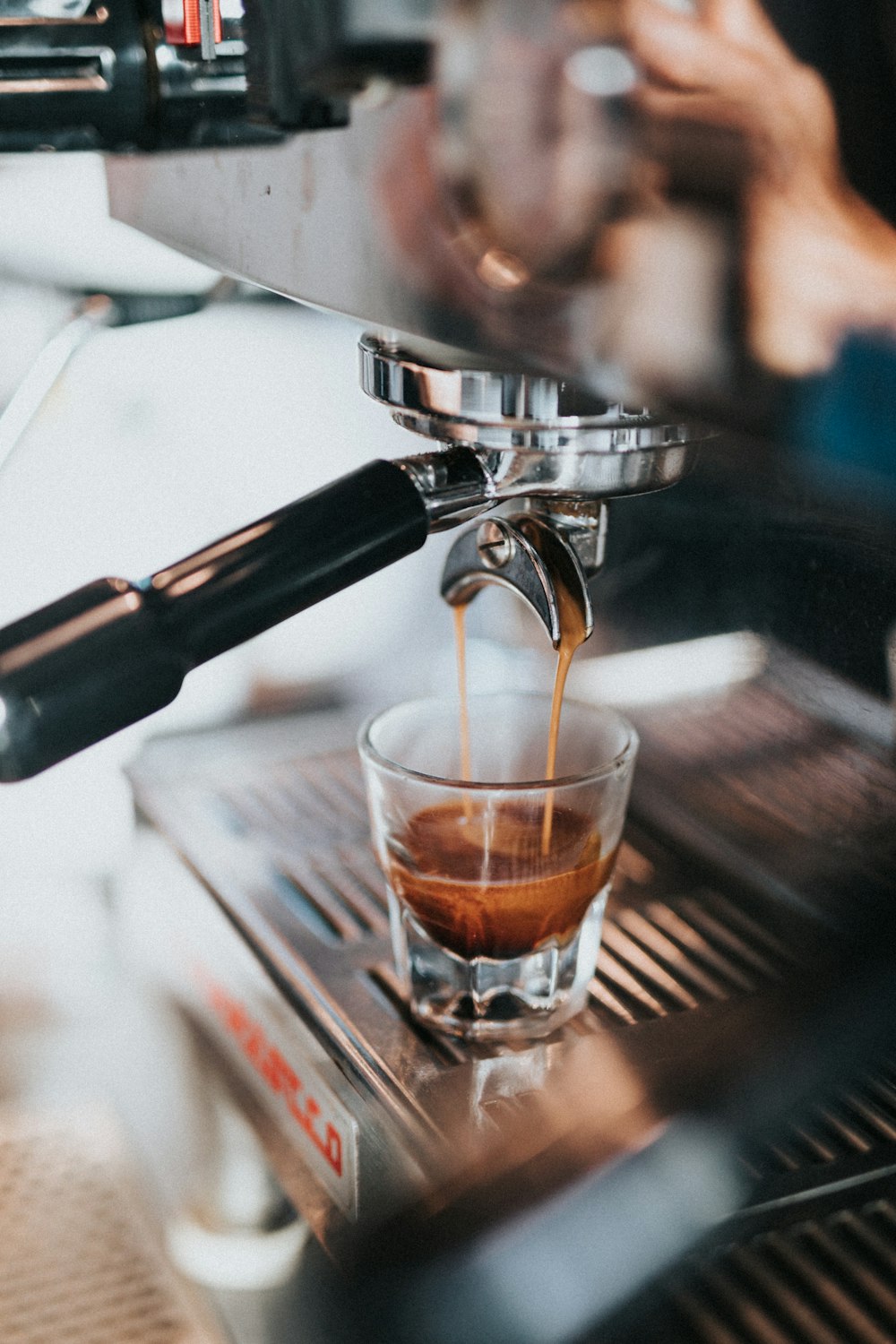 Bicchiere trasparente con liquido marrone su macchina per caffè espresso argento e nero