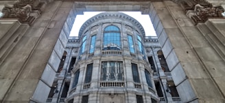 A grand architectural structure with ornate details featuring large arched windows and intricate stone carvings. The building has a classic design with symmetrical elements, framed by a massive arched entrance.