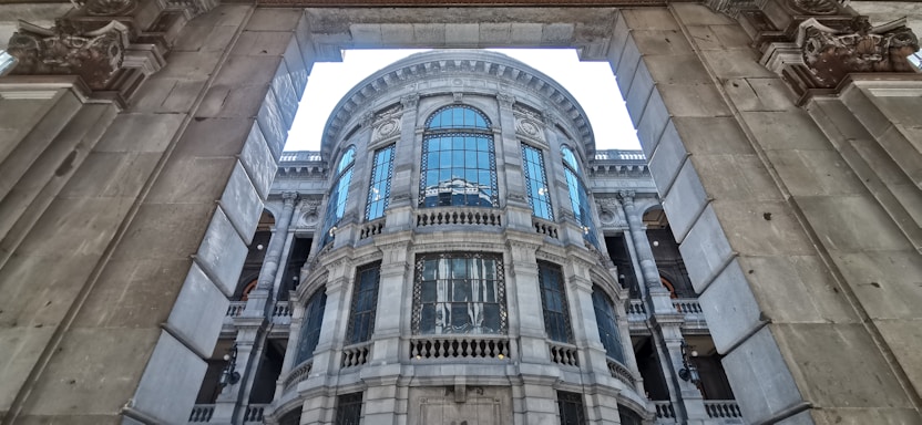 A grand architectural structure with ornate details featuring large arched windows and intricate stone carvings. The building has a classic design with symmetrical elements, framed by a massive arched entrance.