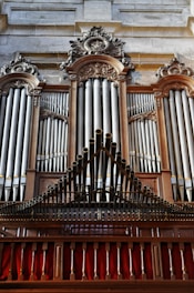 A grand and ornate pipe organ with intricate woodwork and decorative carvings. The pipes are prominently displayed, set within an elegant wooden frame. The structure is majestic and detailed, indicative of craftsmanship often seen in historical or religious settings.