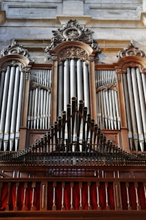 A grand and ornate pipe organ with intricate woodwork and decorative carvings. The pipes are prominently displayed, set within an elegant wooden frame. The structure is majestic and detailed, indicative of craftsmanship often seen in historical or religious settings.