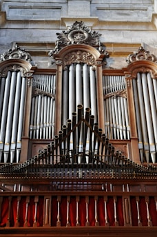 A grand and ornate pipe organ with intricate woodwork and decorative carvings. The pipes are prominently displayed, set within an elegant wooden frame. The structure is majestic and detailed, indicative of craftsmanship often seen in historical or religious settings.