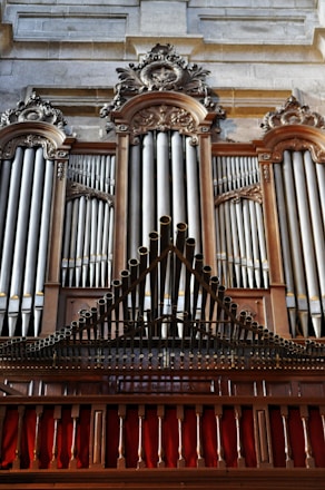 A grand and ornate pipe organ with intricate woodwork and decorative carvings. The pipes are prominently displayed, set within an elegant wooden frame. The structure is majestic and detailed, indicative of craftsmanship often seen in historical or religious settings.