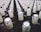 A large collection of glass bottles arranged in rows, each with a beige paper label around the neck featuring a stylized design and text. The tops of the bottles are sealed with metallic caps.