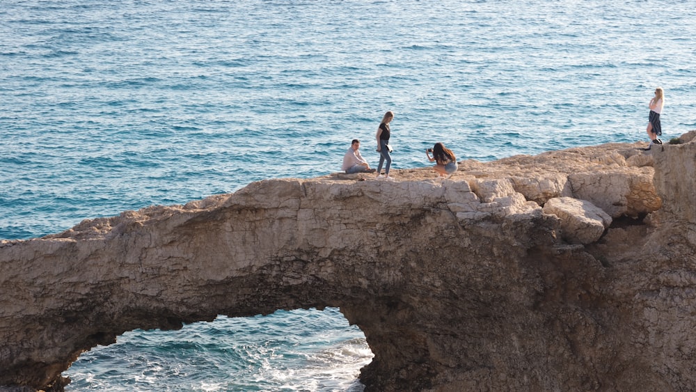 2 person sitting on rock formation near body of water during daytime