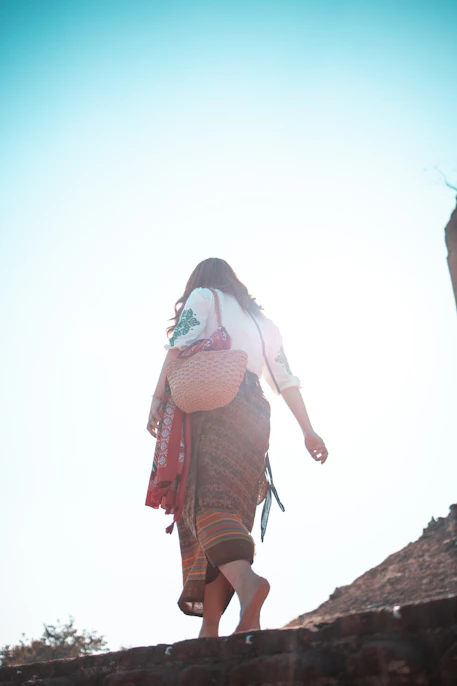 woman in white long sleeve shirt and brown skirt standing on brown rock during daytime