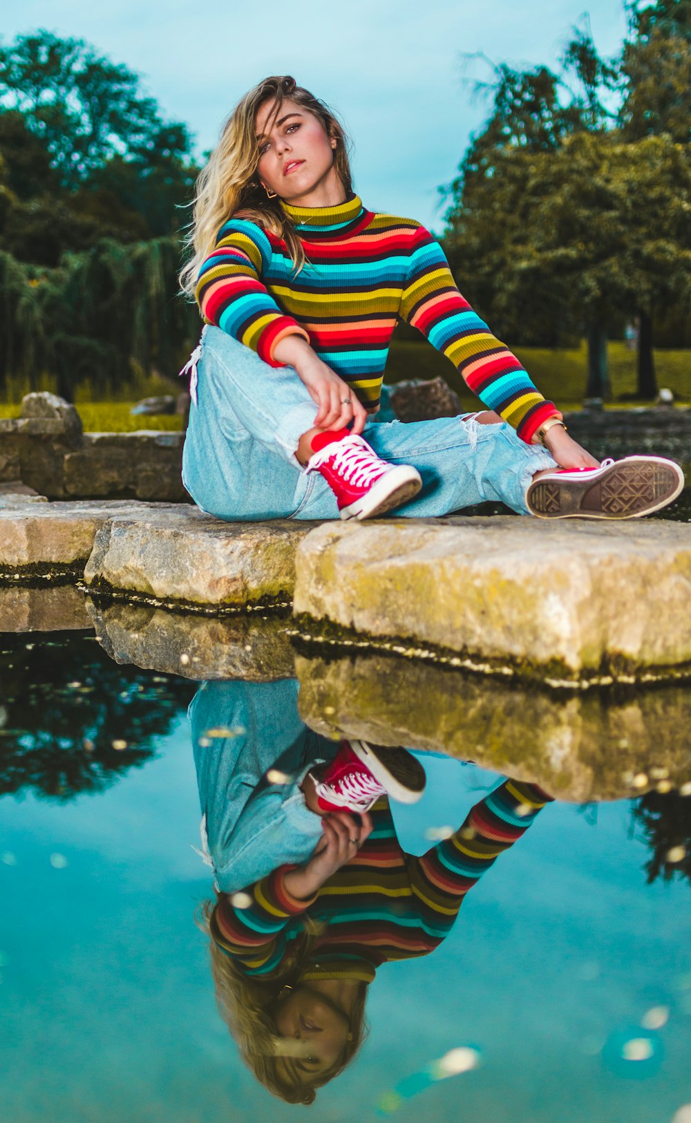 person in blue denim jeans sitting on rock near body of water during daytime