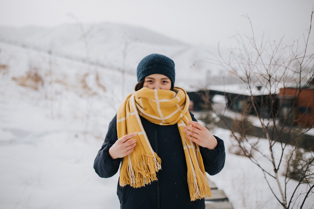 Mujer con gorro de punto negro y chaqueta negra de pie en el suelo cubierto de nieve durante el día