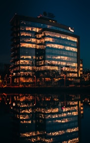 A panoramic view of a modern office building bathed in deep navy blue lighting at dusk.