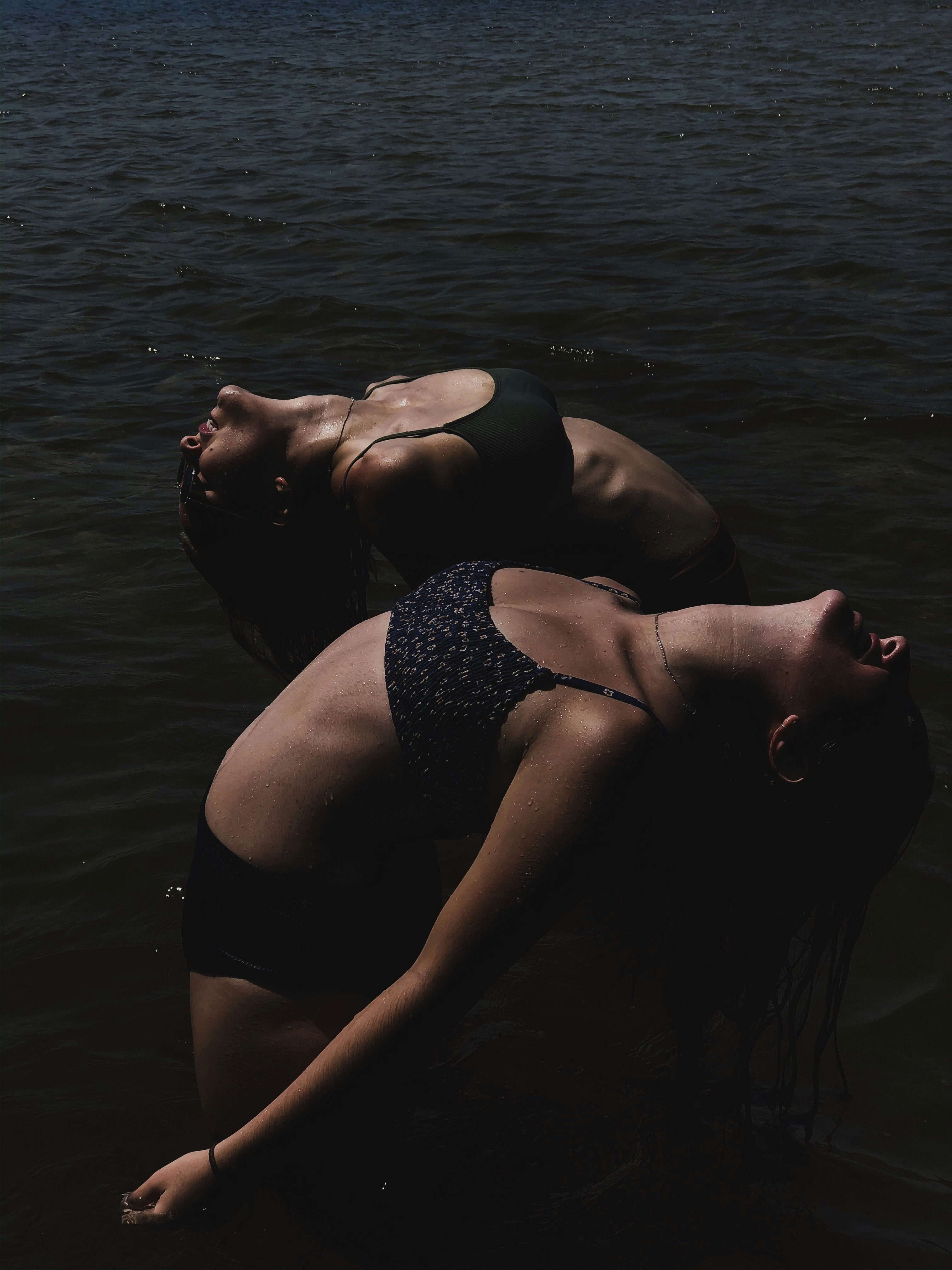 Two women stretching side by side on mats in sunlit studio