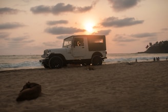 A rugged Jeep Wrangler parked on a sandy beach at sunset.