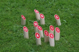 Several wooden blocks with red circular tops, displaying numbers from 1 to 12, are arranged on a grass field.